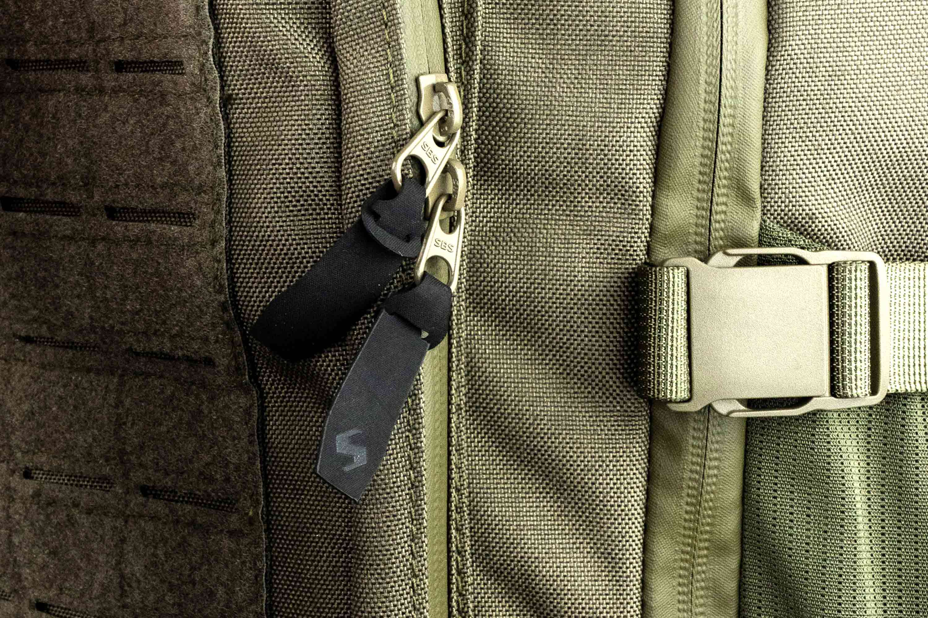 Nahaufnahme eines olivgrünen taktischen Rucksacks aus strapazierfähigem Stoff, SBS-Reißverschlüssen und einer stabilen Seitenschnalle.