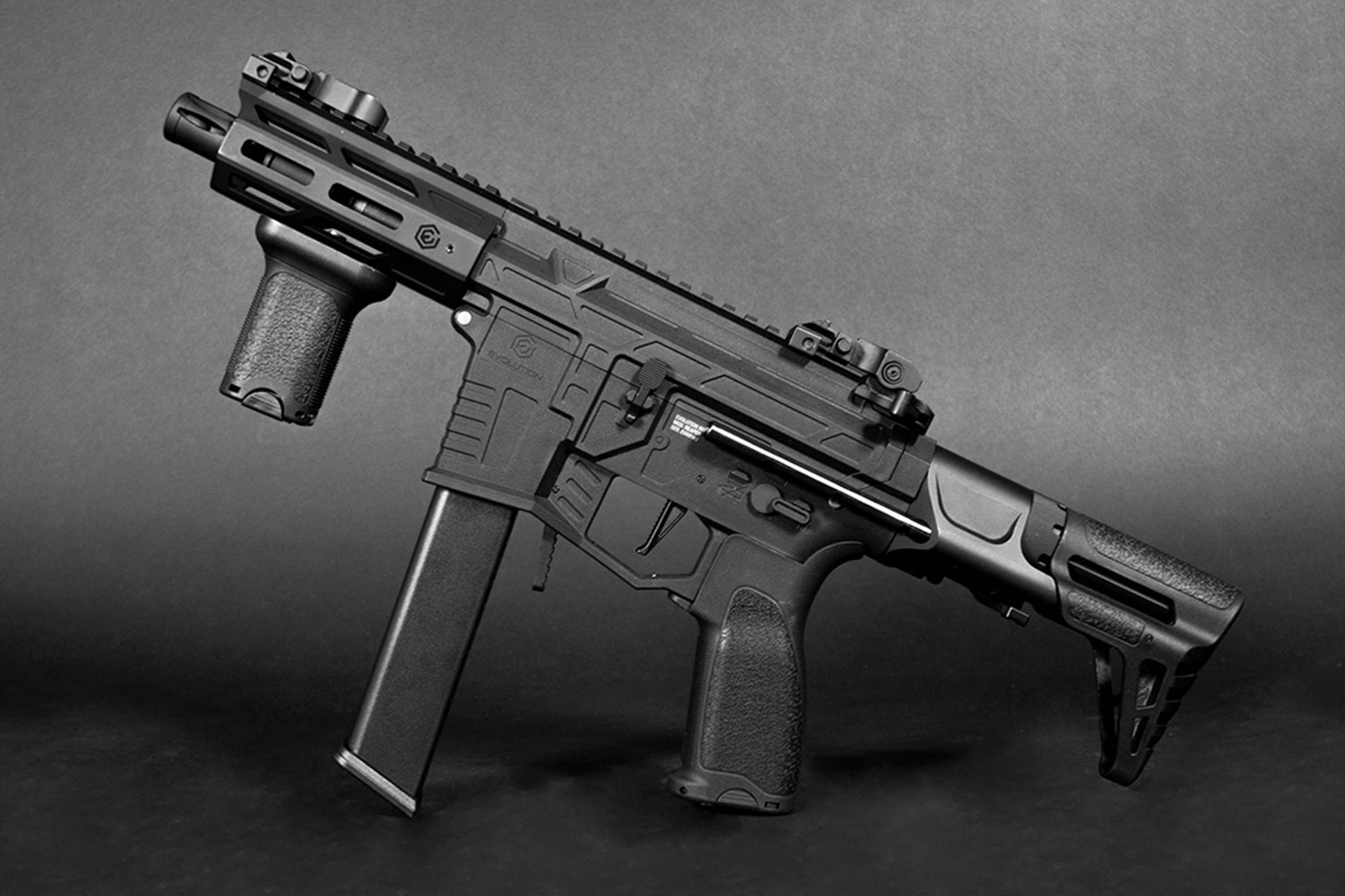 Schwarzer Evolution Airsoft-Karabiner mit taktischem Vordergriff, verstellbarem Schaft und Schienensystem auf dunkelgrauem Hintergrund.