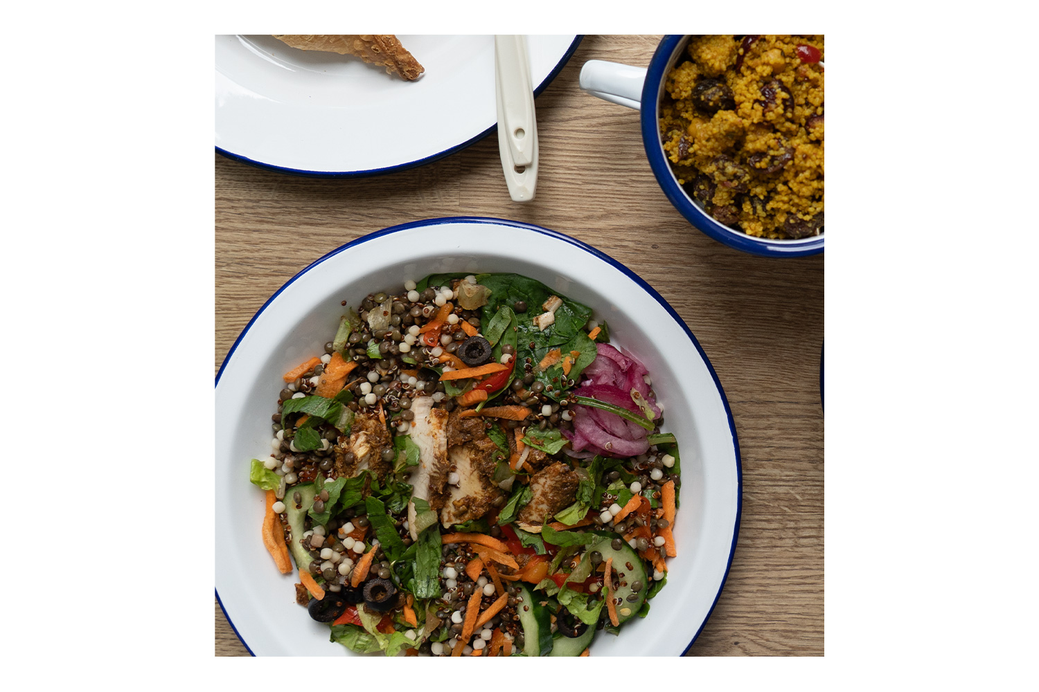 Ein Blick von oben auf einen frischen Salat mit Hühnchen, Linsen und Gemüse, serviert in einer weißen Emailleschüssel mit blauem Rand.