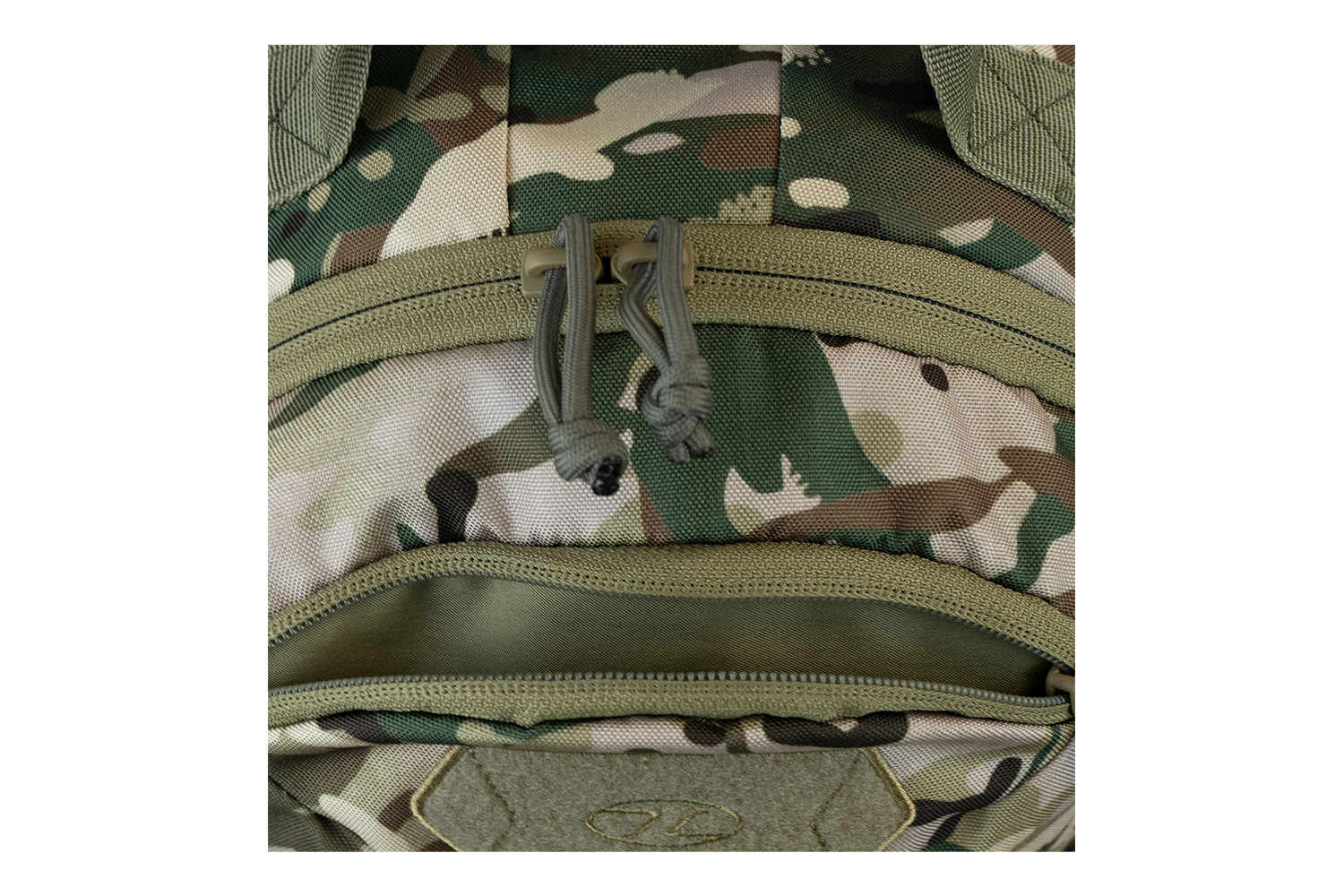 Nahaufnahme eines taktischen Rucksacks im Tarnmuster mit olivgrünen Reißverschlüssen, Zugschnüren und einem Klettverschlussbereich.