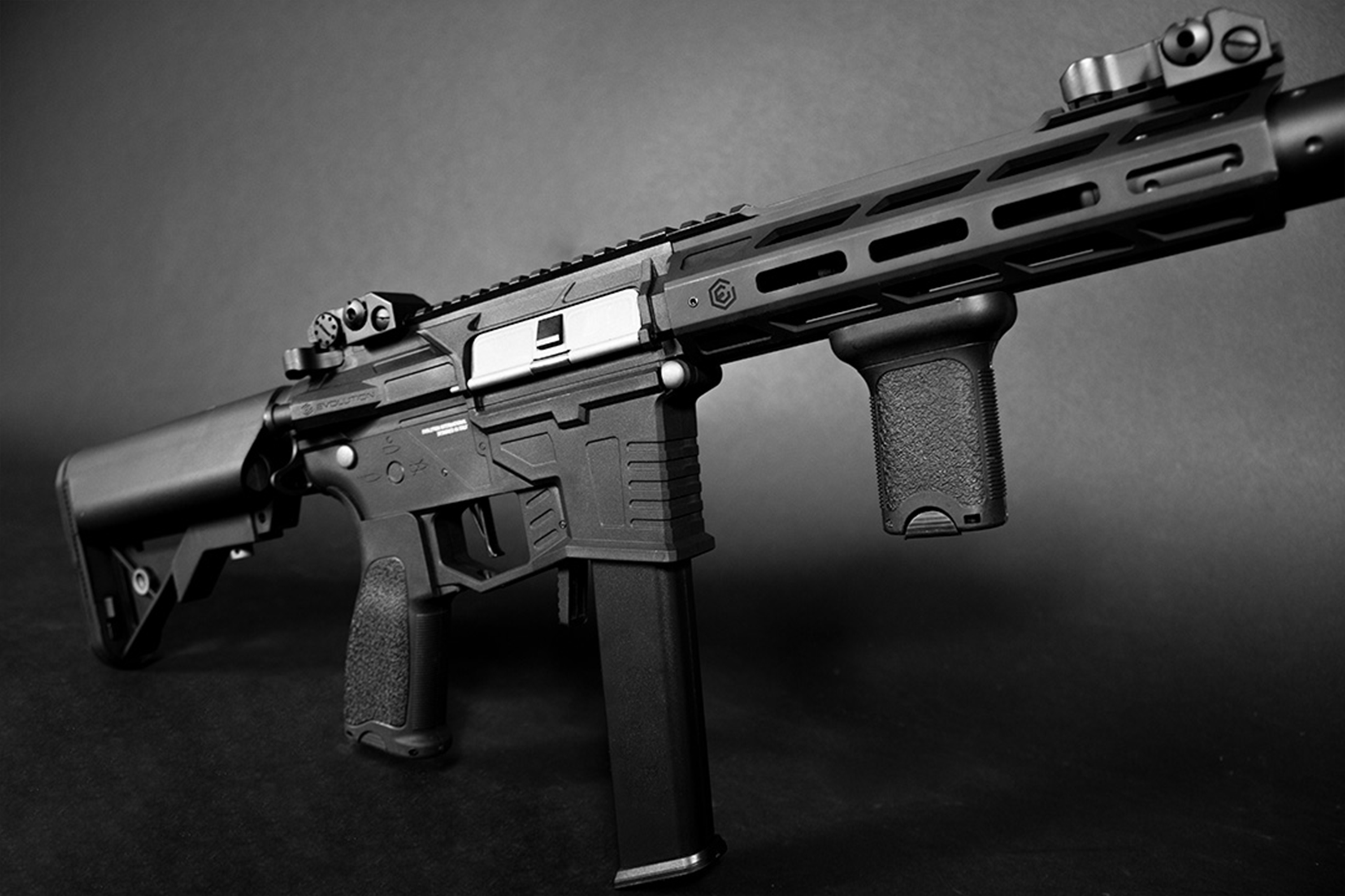 Schwarzes Evolution-Airsoftgewehr mit taktischem Handschutz, vertikalem Griff und verstellbarem Schaft auf dunklem Hintergrund.