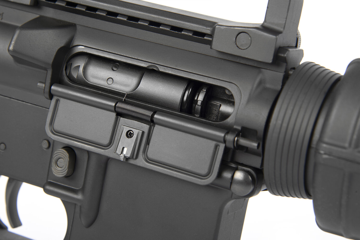 Nahaufnahme eines schwarzen Luftgewehrgehäuses im AR-15-Stil mit offener Staubschutzhülle, die den internen Bolzenträgermechanismus zeigt.