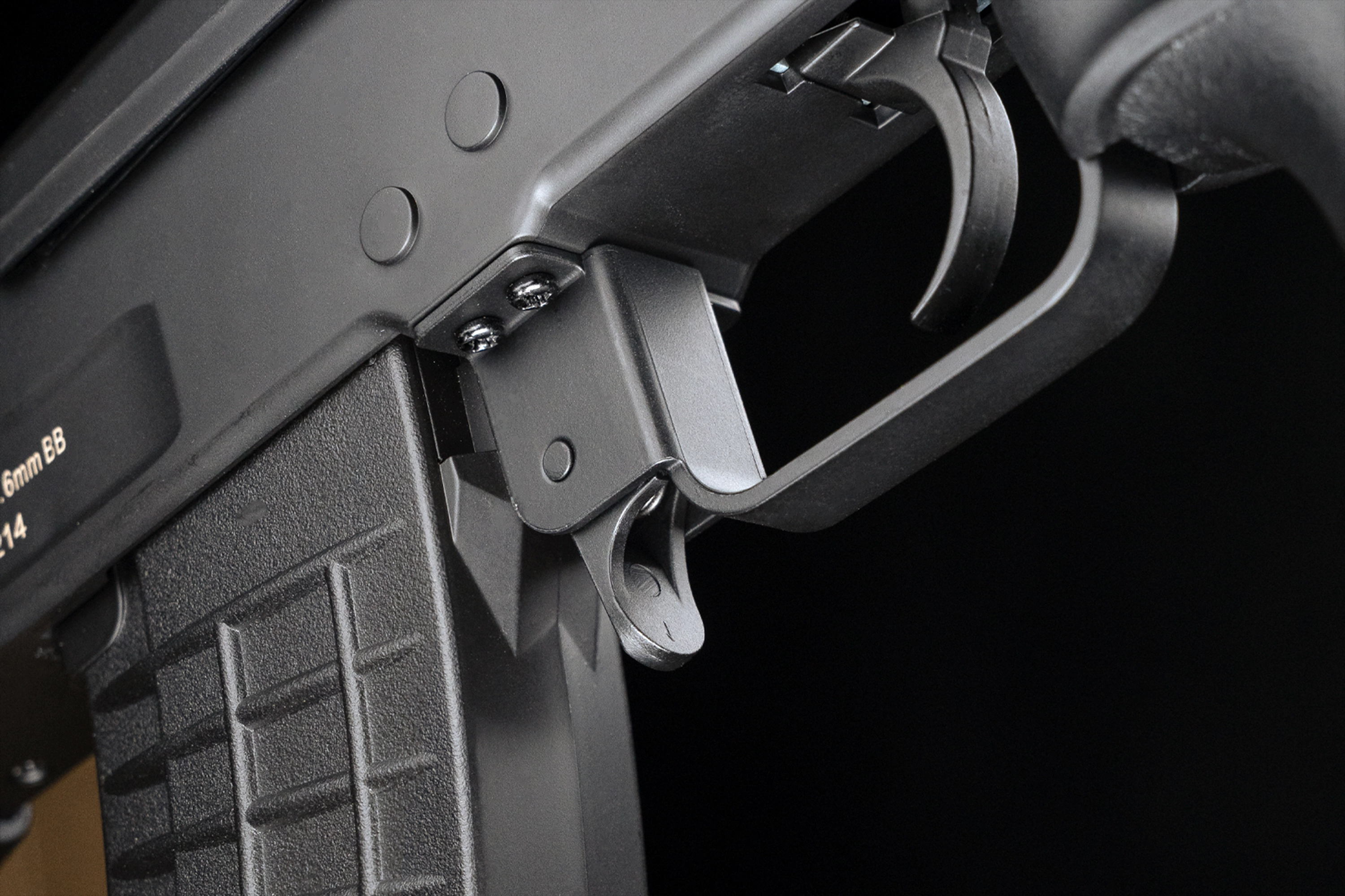 Nahaufnahme eines schwarzen Luftgewehr-Abzugsbügels und Magazinauslösehebels an einem taktischen Schusswaffenzubehörteil.