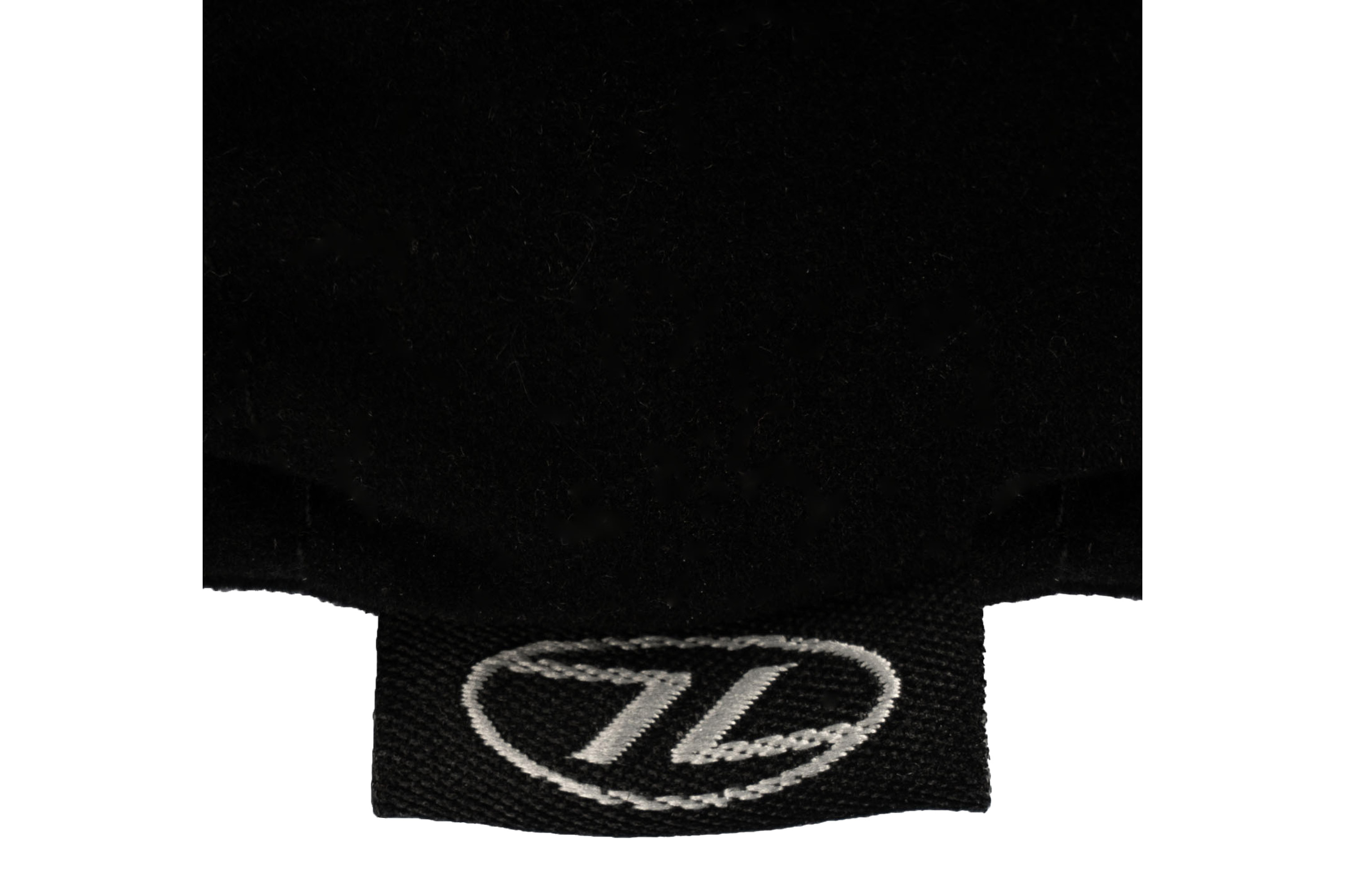 Nahaufnahme eines schwarzen Stoffaccessoires mit einem kleinen, gestickten Etikett mit einem weißen ovalen Logo und den Buchstaben TL.