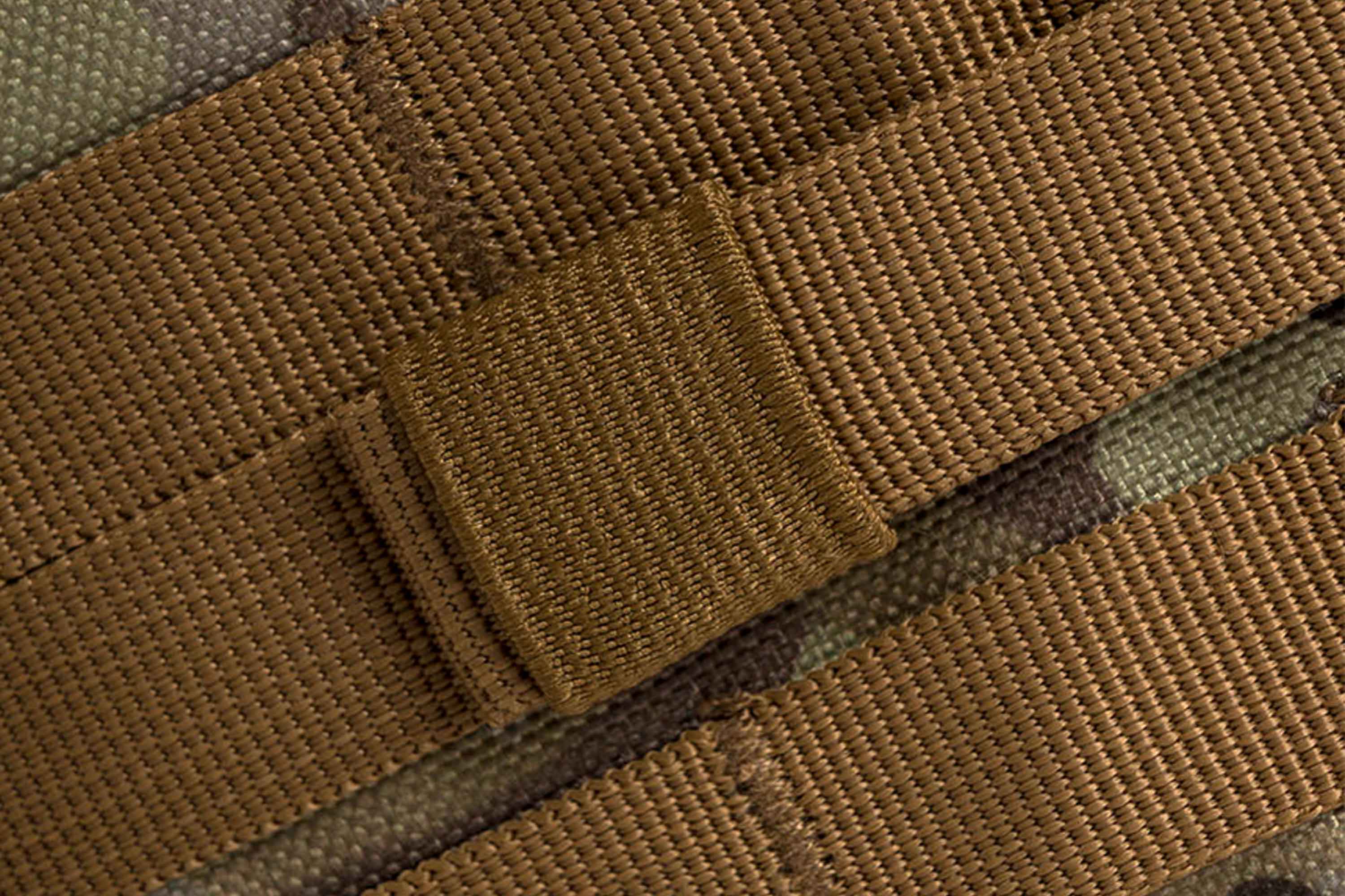 Nahaufnahme von strapazierfähigen braunen Nylon-Gurtbändern mit einem verstärkten elastischen Halter auf einer getarnten Oberfläche für taktische Ausrüstung.