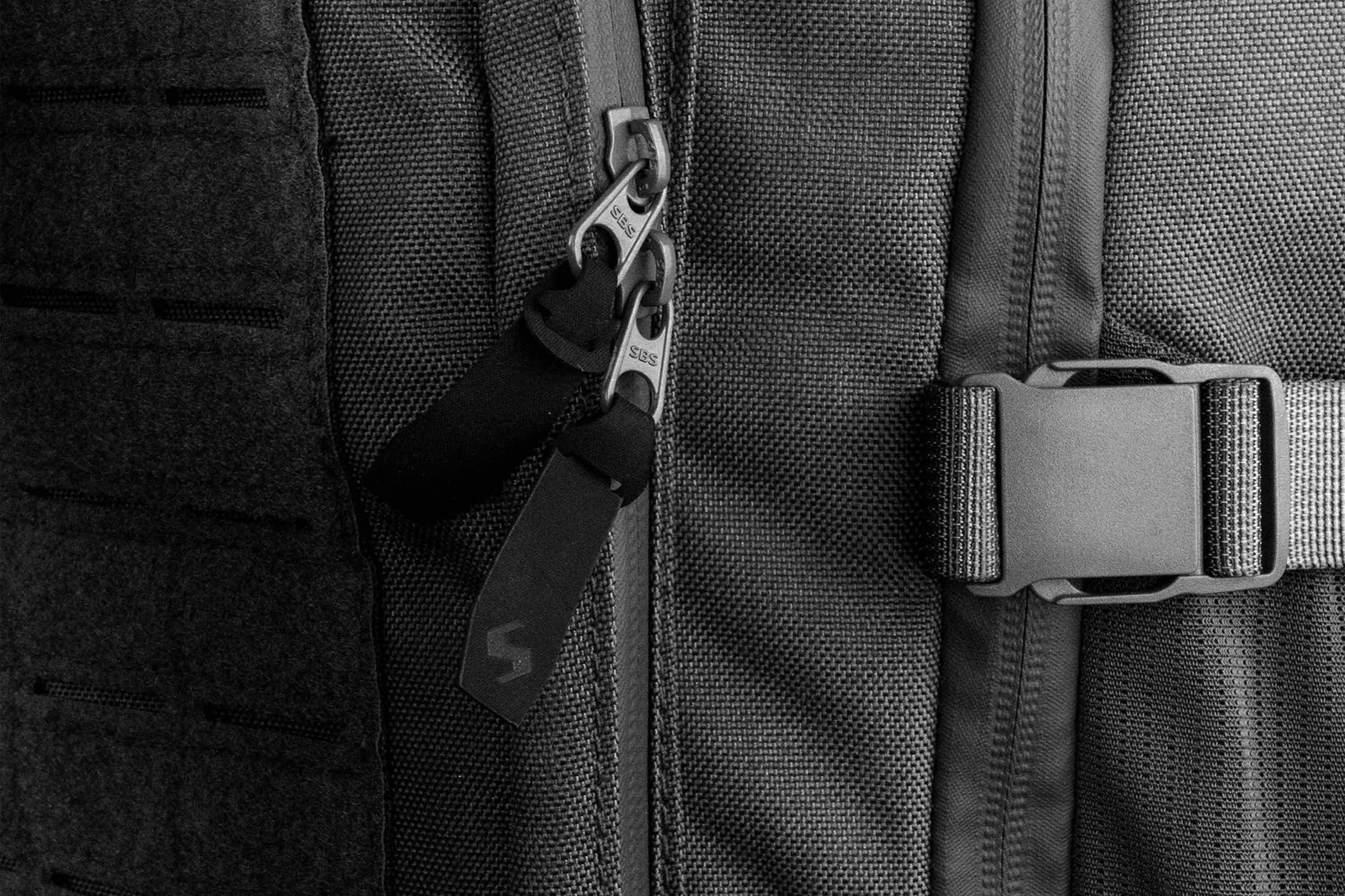 Nahaufnahme eines schwarzen taktischen Rucksacks aus strapazierfähigem Stoff, SBS-Reißverschlüssen und einer stabilen seitlichen Schnalle.
