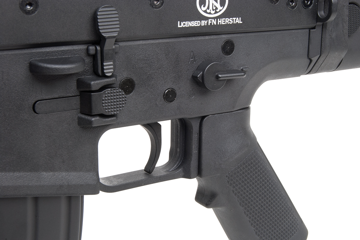 Nahaufnahme des schwarzen Polymergehäuses, des Abzugs und des Sicherheitswahlschalters an einem von FN Herstal lizenzierten Airsoft-Gewehr.