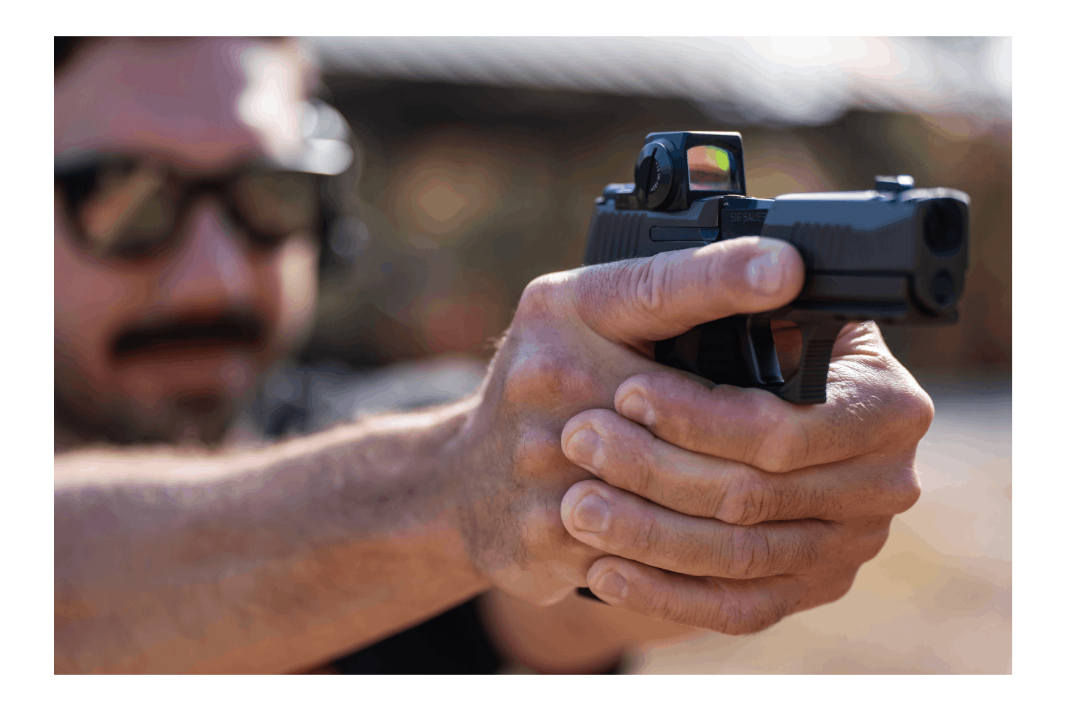 Ein Schütze zielt mit einer schwarzen Sig Sauer-Pistole, die mit einem Leuchtpunktvisier ausgestattet ist, und hält sie mit beiden Händen auf Distanz fest.