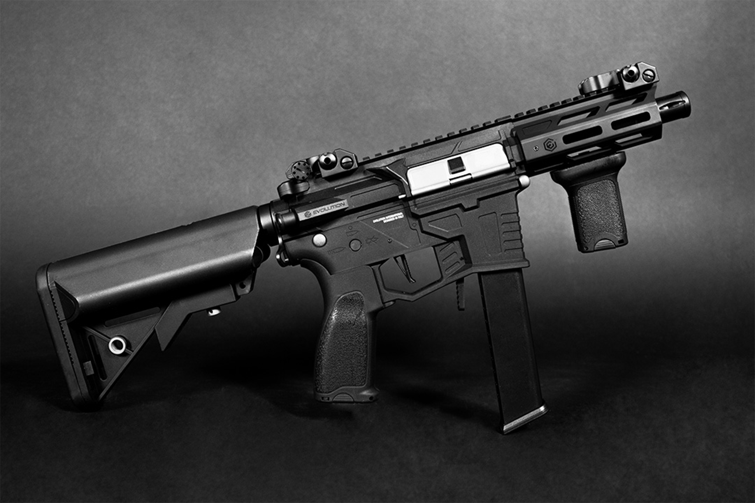 Evolution Airsoft-Karabinergewehr in Schwarz mit taktischem Schaft, vertikalem Vordergriff und Schienensystem auf dunklem Hintergrund.