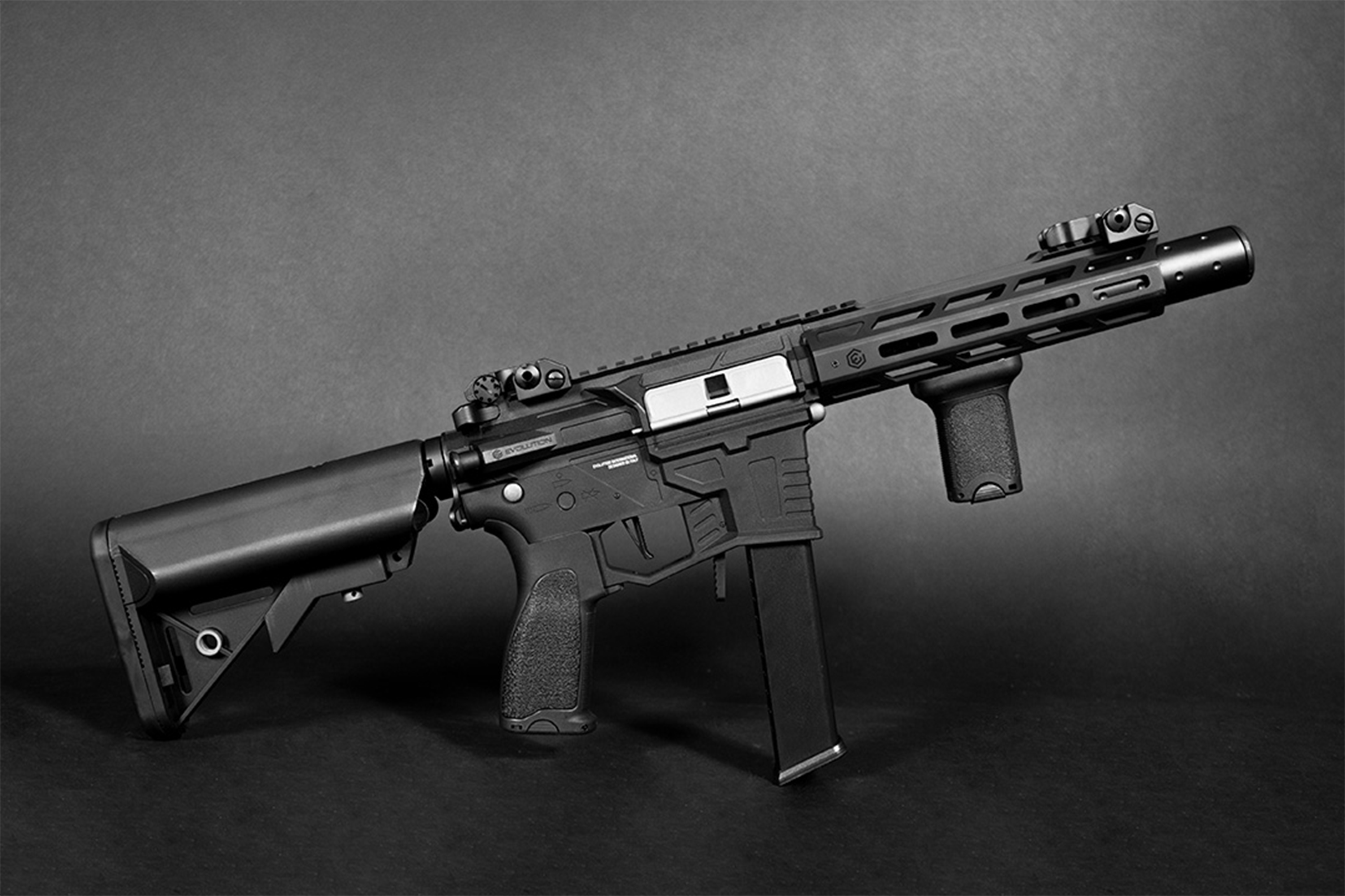 Schwarzer Evolution-Airsoft-Karabiner mit M-LOK-Handschutz, verstellbarem Schaft, vertikalem Griff und Visier auf dunklem Hintergrund.