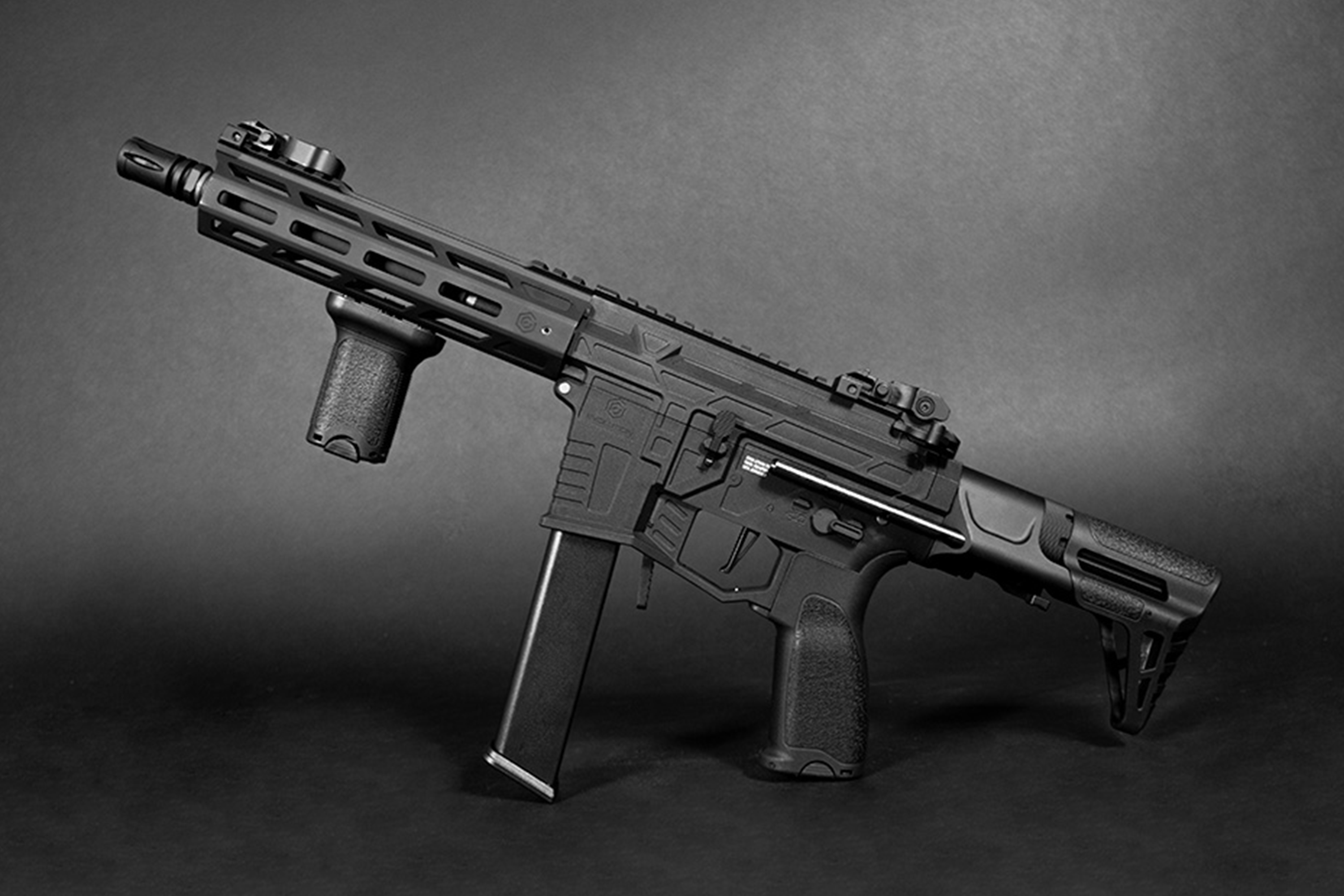 Schwarzer taktischer Airsoft-Karabiner mit vertikalem Vordergriff, langem Magazin und verstellbarem Schaft auf dunklem Hintergrund.